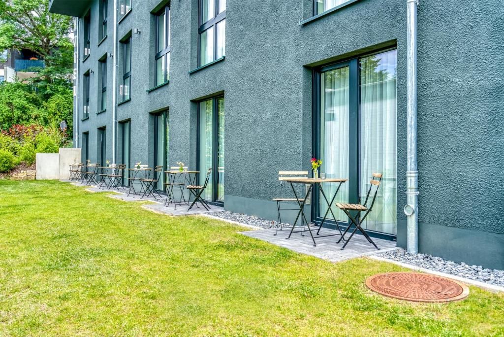 A modern building with a flat roof, large windows, and a paved outdoor area with tables and chairs.