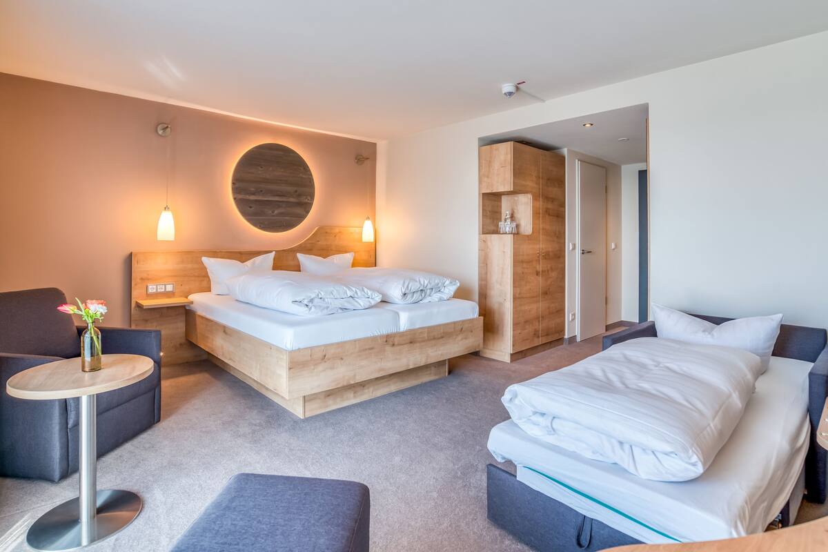 A modern hotel room with a large bed, a smaller bed, a desk, and a chair.