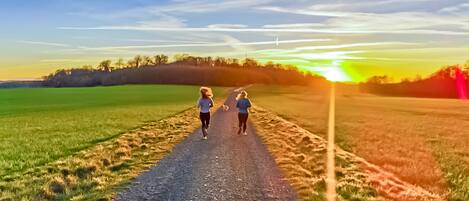 Dos personas corriendo por un camino de grava, rodeado de campos.