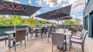An outdoor patio with wicker furniture and large umbrellas, overlooking a body of water. - Hotel Beckmann (Goettingen)