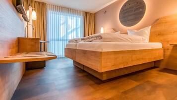 A modern hotel room with a bed, a wooden bedside table, a built-in bench, and a large window with curtains.