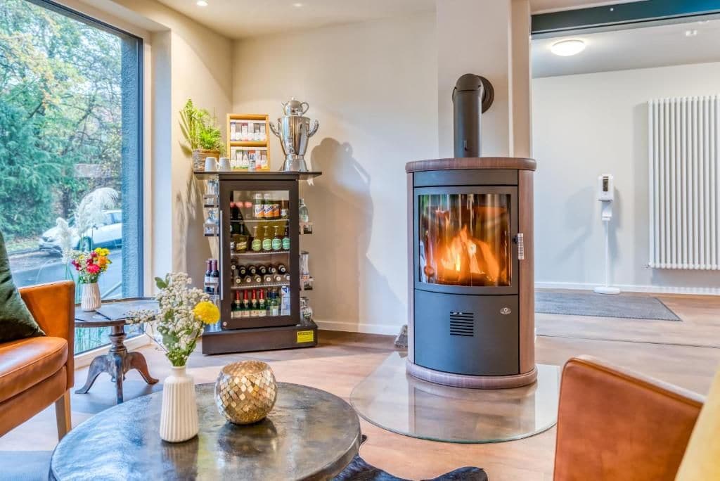 A modern living room with a wood-burning stove, a glass-top coffee table, and a bookshelf with various items.