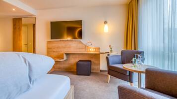 A hotel room with a bed, a desk, a chair, and a small table with a bottle and glass.
