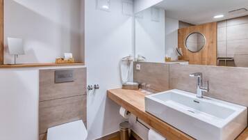 Un baño moderno con un espejo grande, un lavamanos blanco y un inodoro.