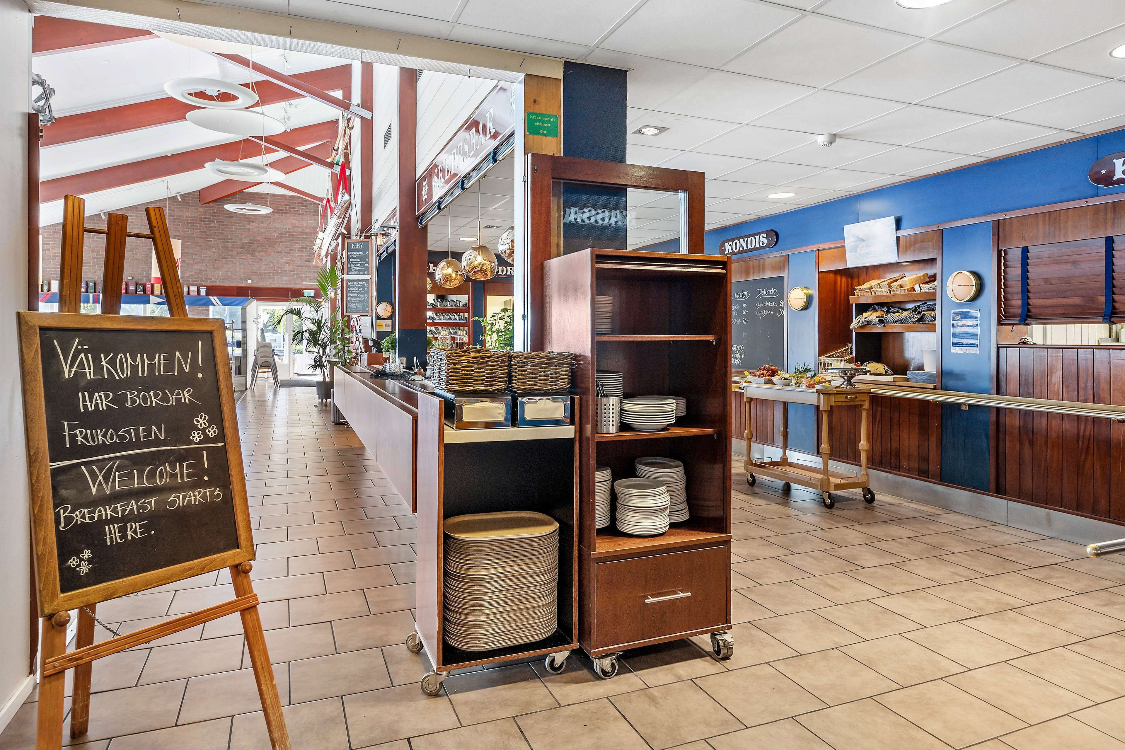 L’intérieur d’un restaurant, avec un panneau noir, un comptoir de buffet et un chariot en bois sur lequel sont empilées des assiettes.