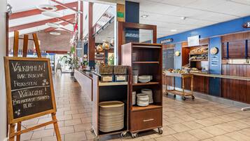 L’intérieur d’un restaurant, avec un panneau noir, un comptoir de buffet et un chariot en bois sur lequel sont empilées des assiettes.
