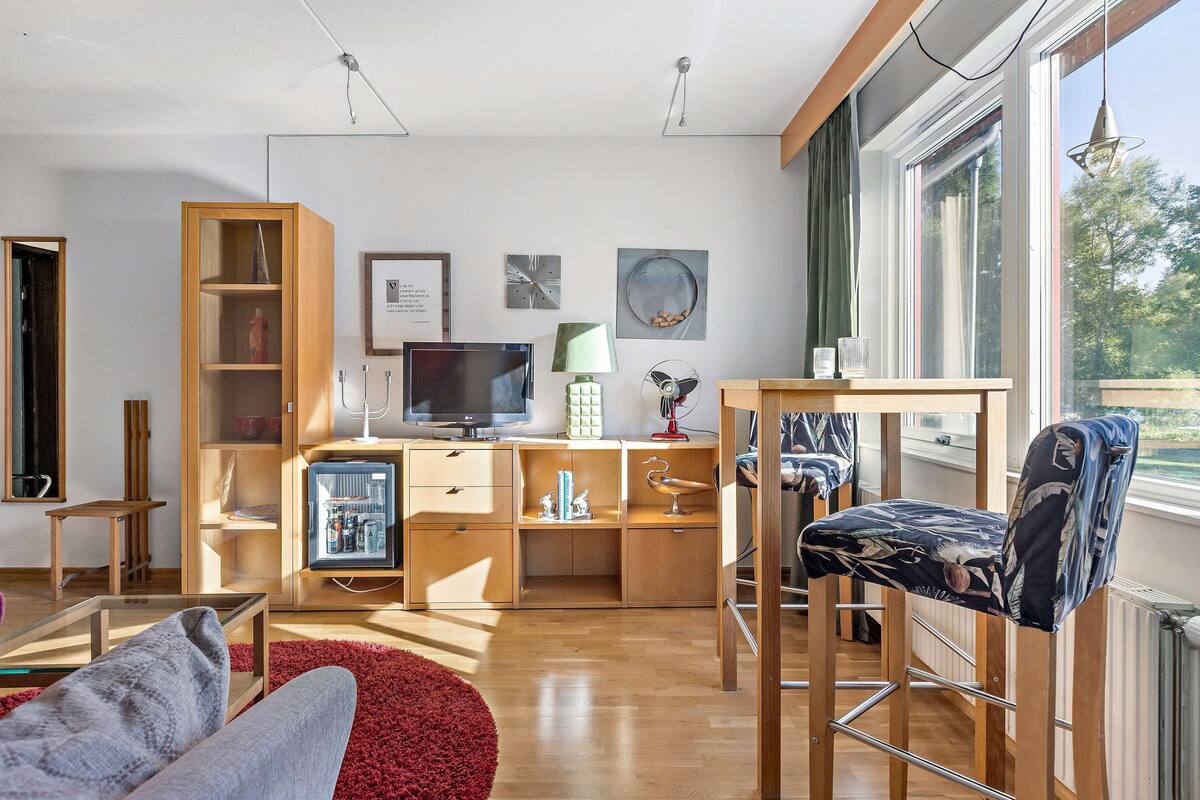 Una sala de estar moderna con televisor, muebles de madera y ventanas amplias.
