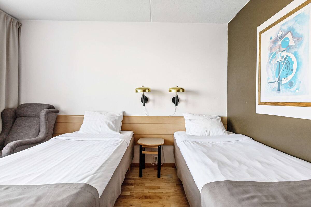 Una habitación de hotel con dos camas individuales, una mesita, una silla y dos lámparas de pared.