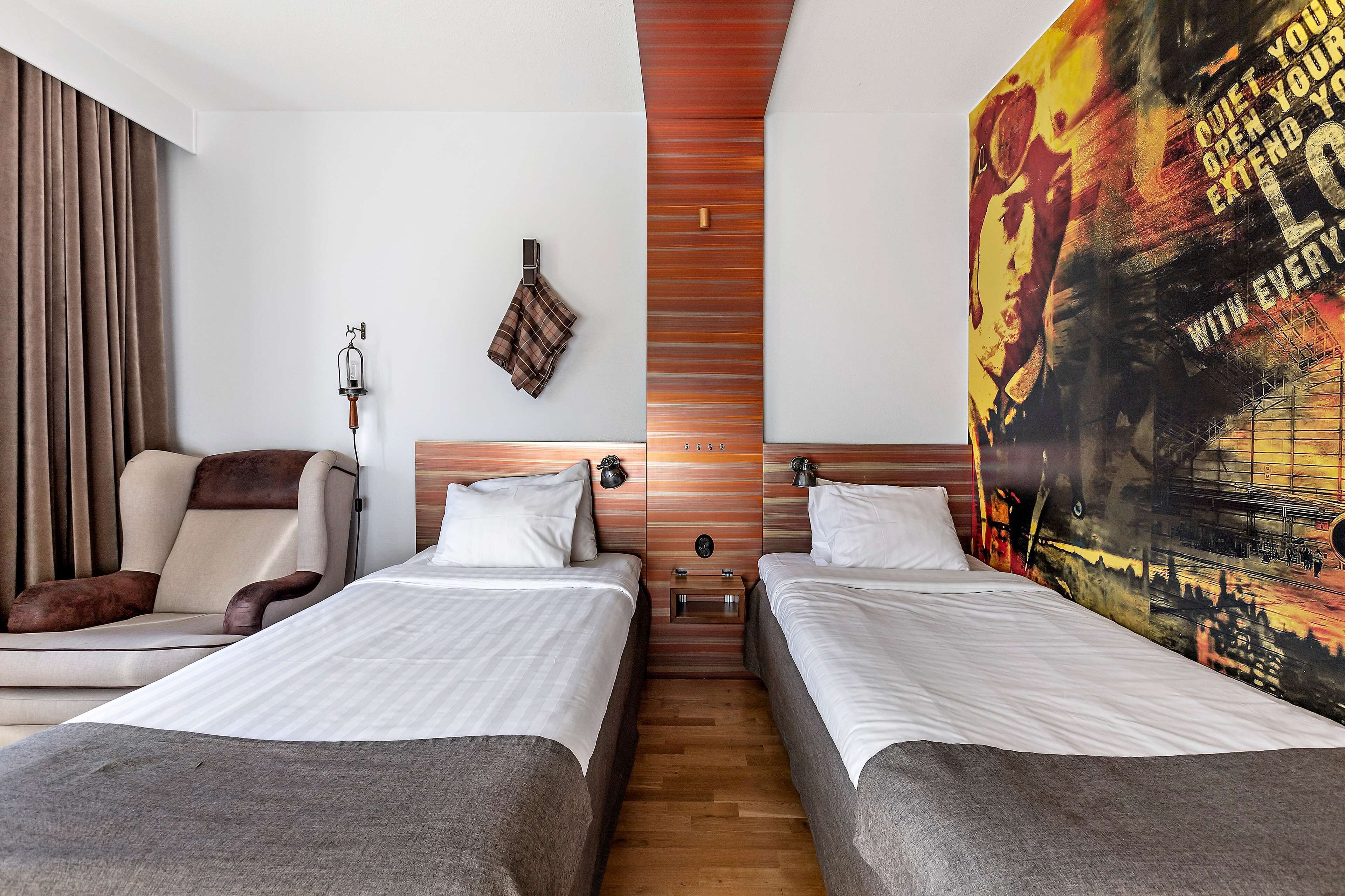 Habitación de hotel con dos camas, un sofá, un muro decorativo de madera y un cartel grande en la pared.