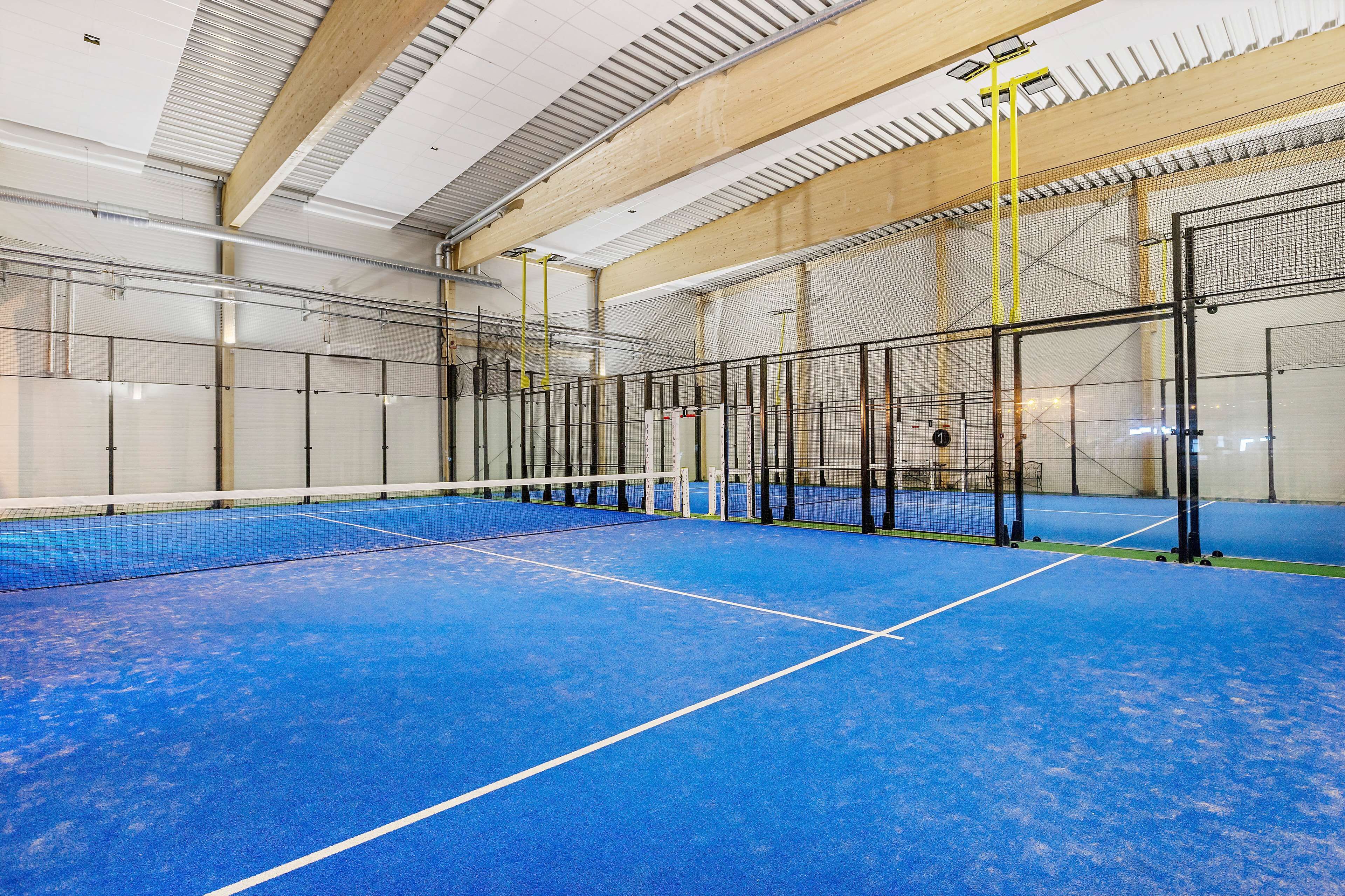 Una cancha de tenis interior con piso azul, delimitada por una red y vallas metálicas.