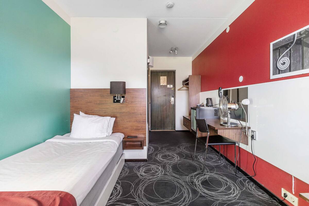 Habitación de hotel con cama, escritorio, espejo, armario y puerta que da a un baño.