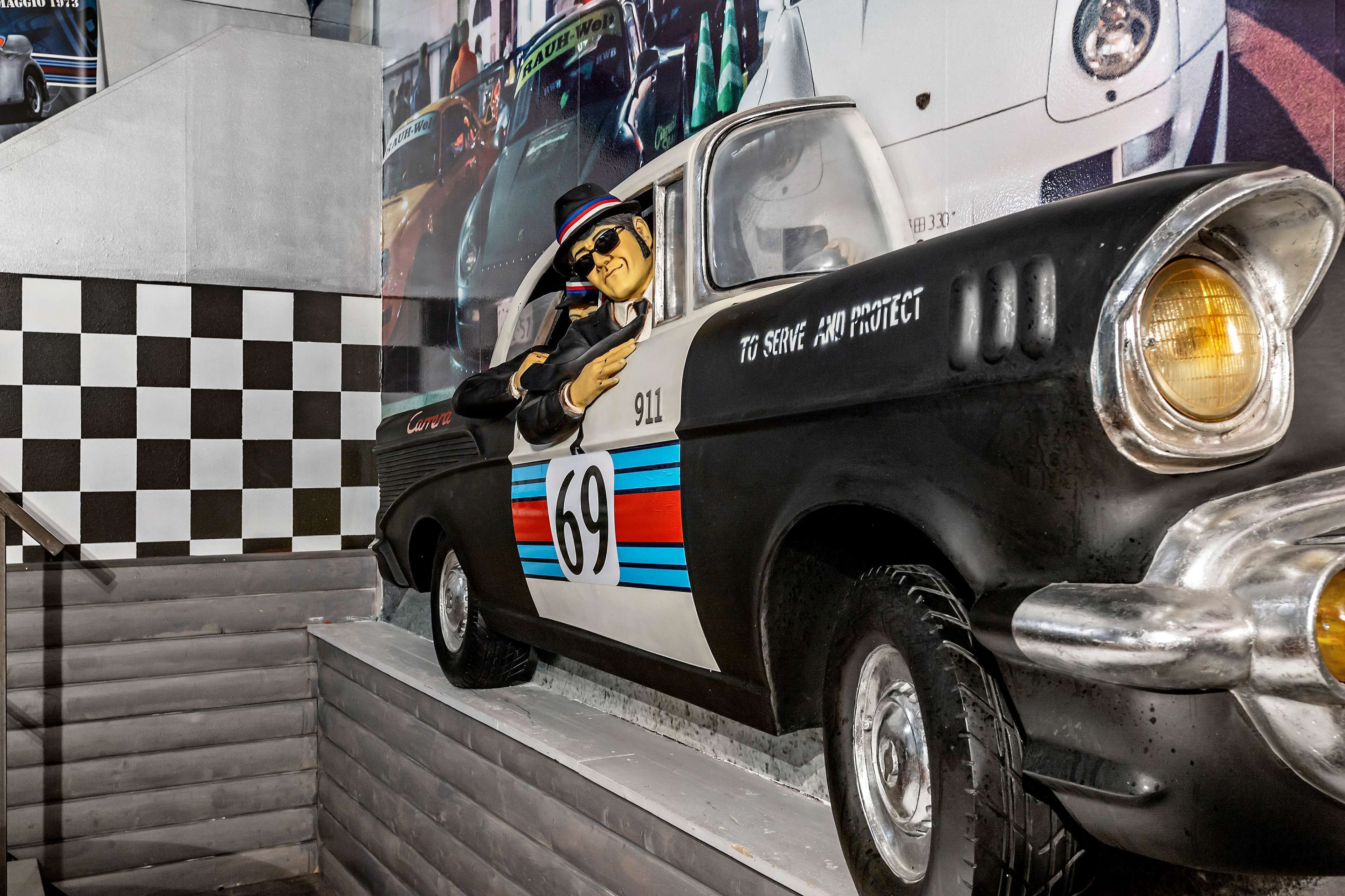 A vintage car with a checkered pattern on the wall behind it.
