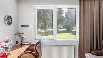 A modern room with a wooden desk, a red fan, a clock, a window with a view of a green landscape, and a white radiator.