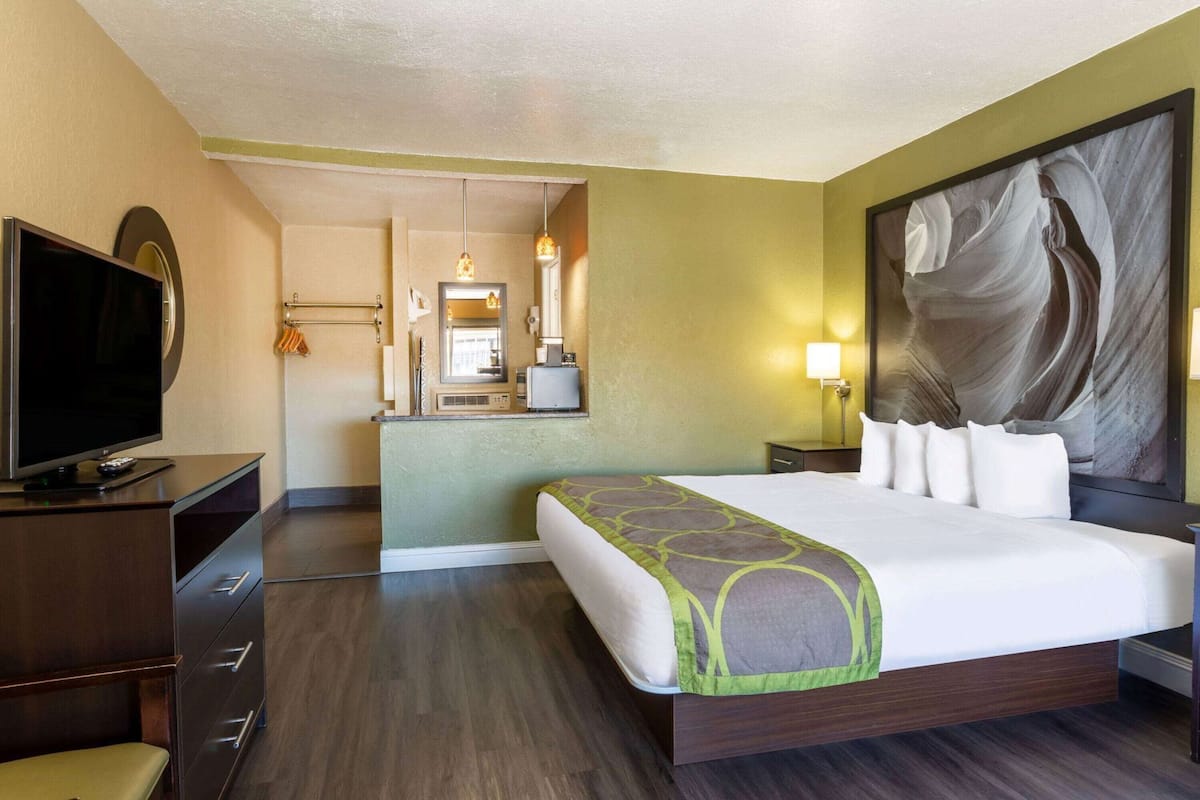 Une chambre d’hôtel avec un grand lit, une télévision, un bureau et une salle de bain visible par une porte ouverte.