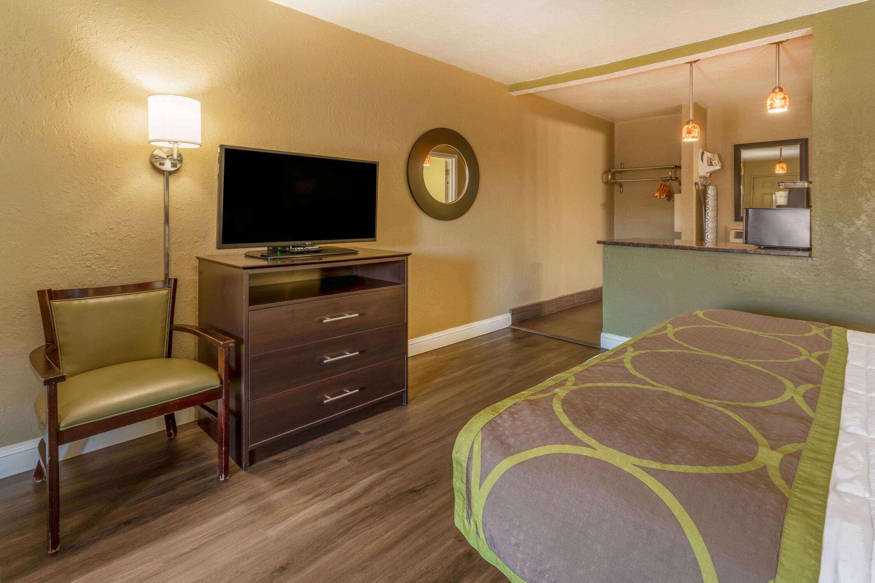 A hotel room with a bed, a TV on a dresser, a chair, and a mirror.
