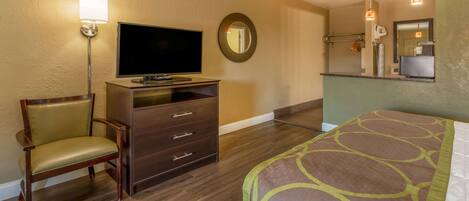 A hotel room with a bed, a TV on a dresser, a chair, and a mirror.