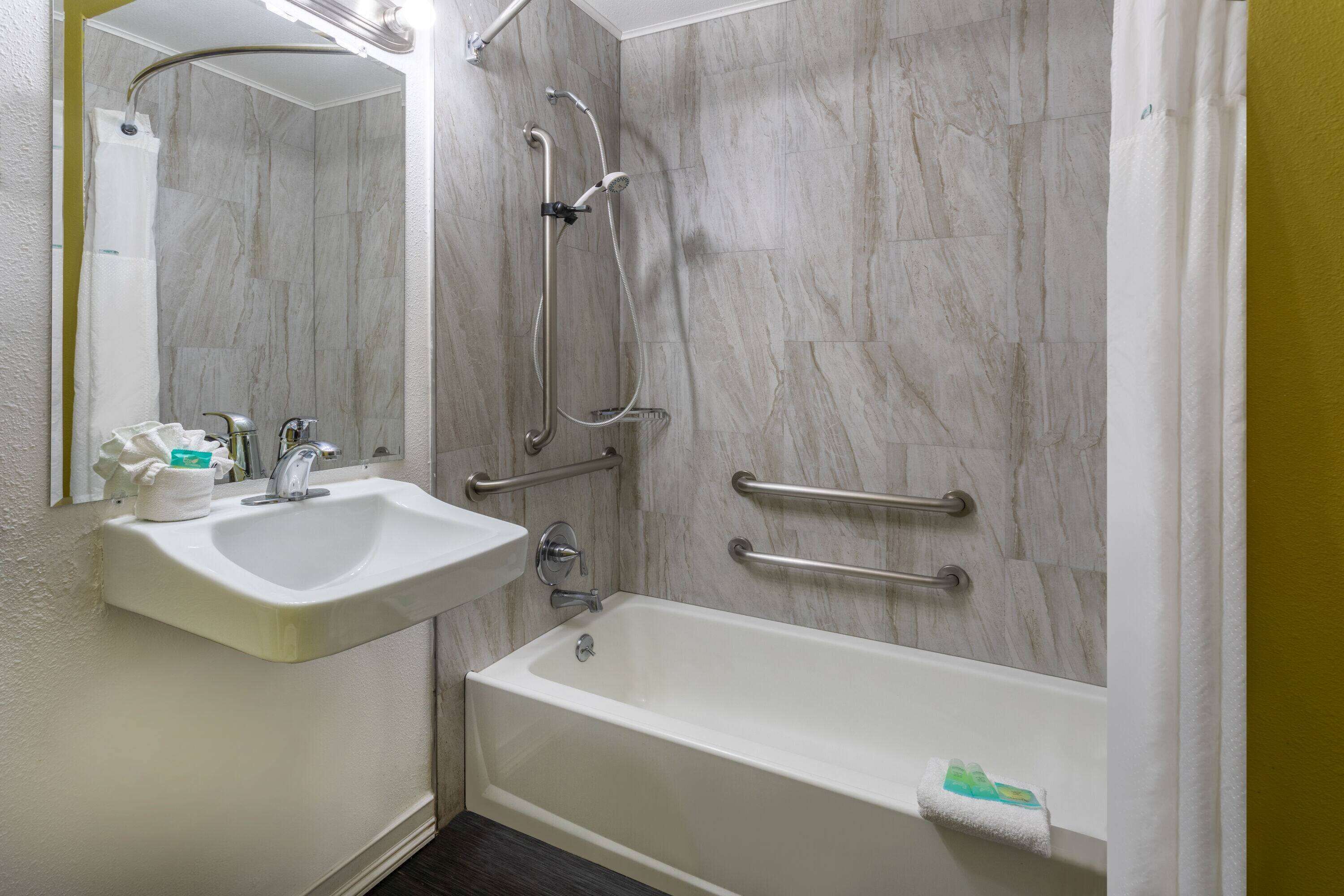 Une salle de bain avec un lavabo blanc, une baignoire et une douche équipée de barres d’appui.
