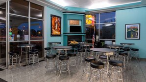 A bar area with multiple stools and tables, a fireplace, and large windows with artwork. - Super 8 by Wyndham Conference Center NAU/Downtown (Flagstaff)
