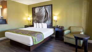 A hotel room with a large bed, two bedside tables with lamps, a chair, and a small table. - Super 8 by Wyndham Conference Center NAU/Downtown (Flagstaff)