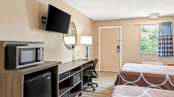 Una habitación de hotel con cama, escritorio, silla, televisor y refrigerador.