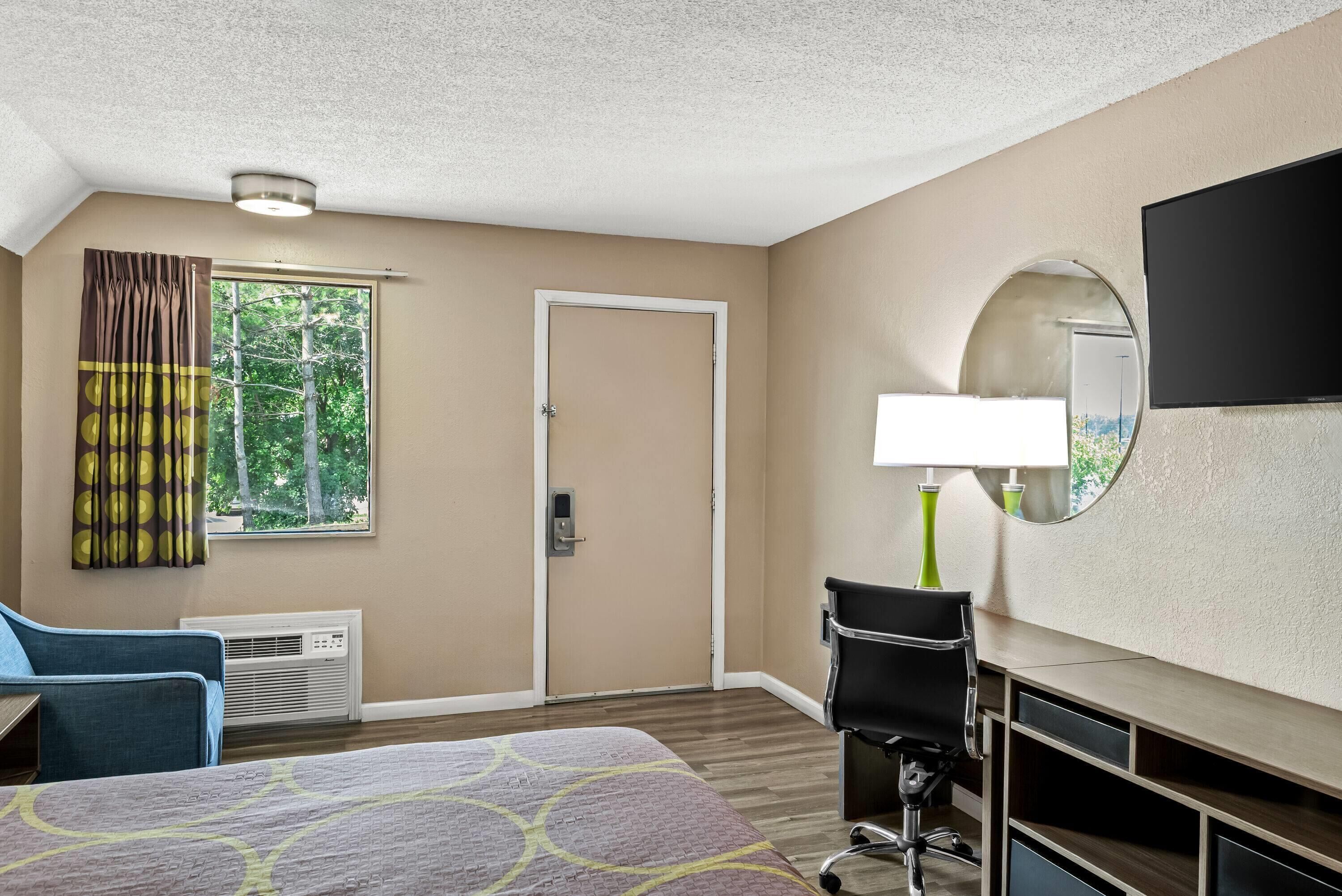 A hotel room with a bed, a desk with a chair, a TV, and a window with curtains.