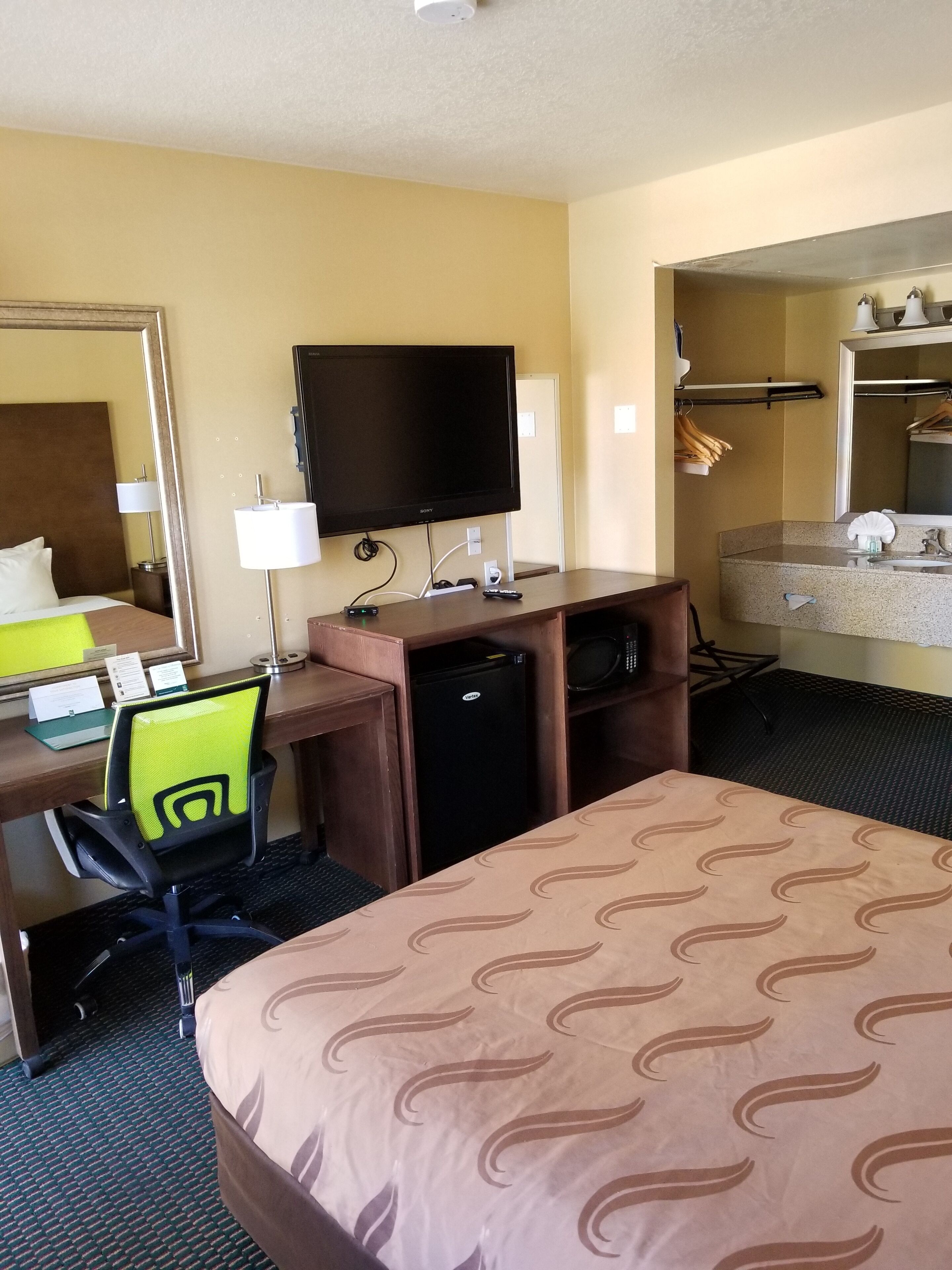 A hotel room with a bed, desk, chair, TV, and a small refrigerator.