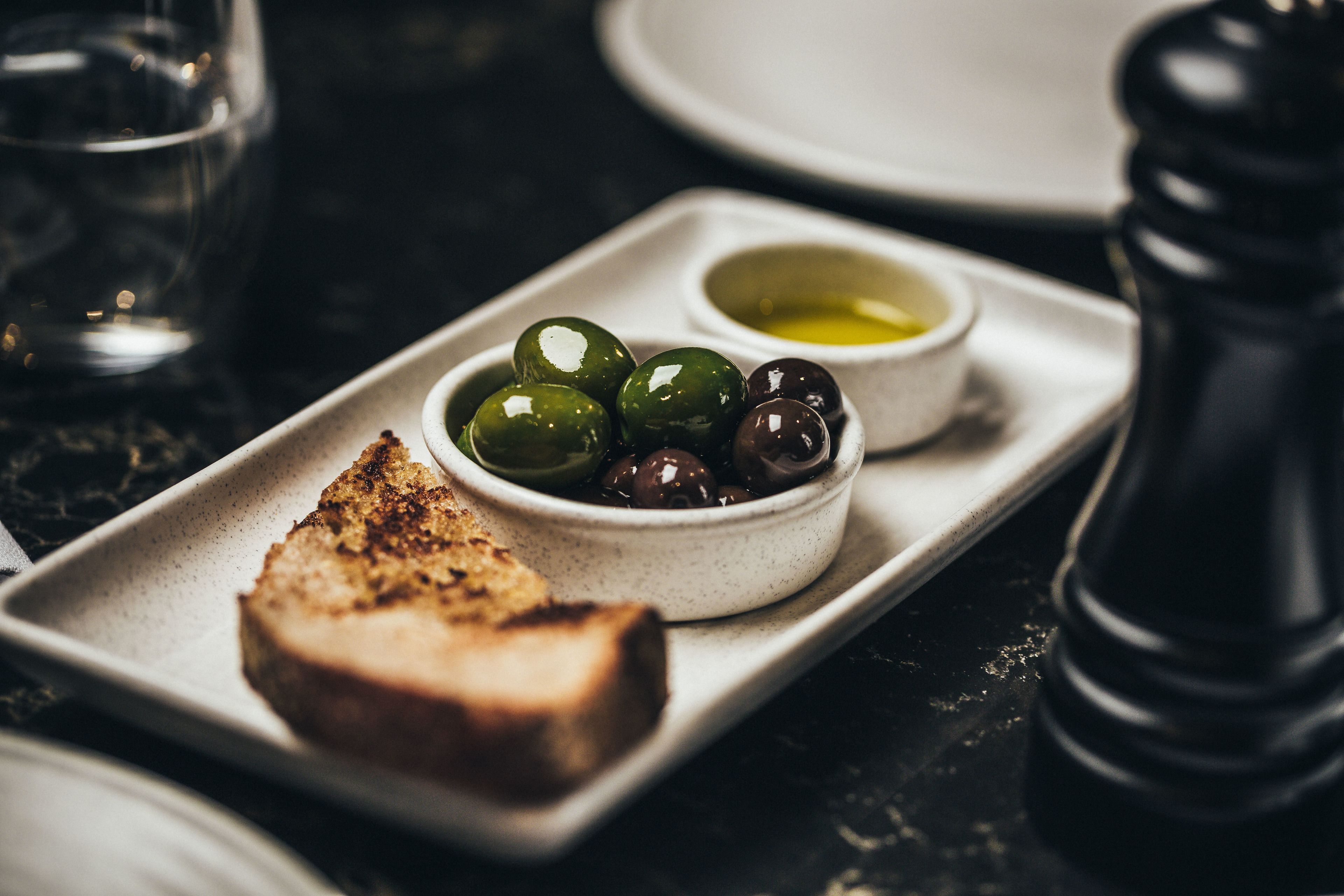 A tray with toasted bread, green and black olives, and a small bowl of olive oil.