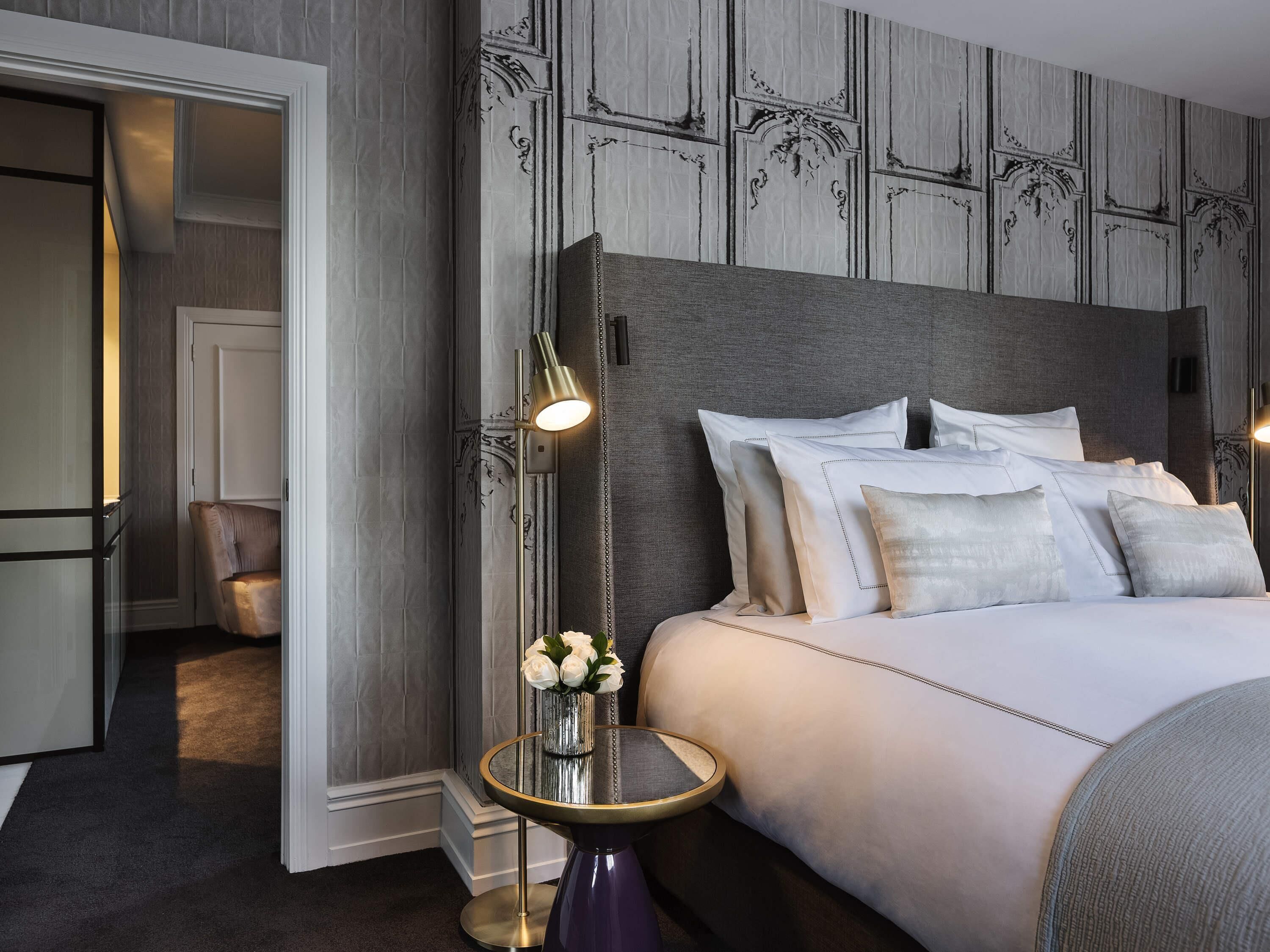 A hotel room with a large bed, a bedside table with a lamp, a chair, and a vase with flowers.
