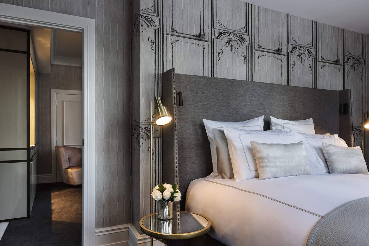 A hotel room with a large bed, a bedside table with a lamp, a chair, and a vase with flowers.