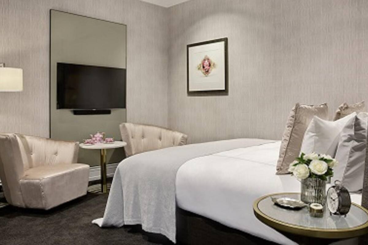 A hotel room with a bed, a chair, a small table with a vase of flowers, a clock, and a television.