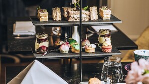 A three-tiered dessert display with various pastries and small dishes, a teapot, and a cup of tea on a table. - Fable Auckland, MGallery (Auckland)