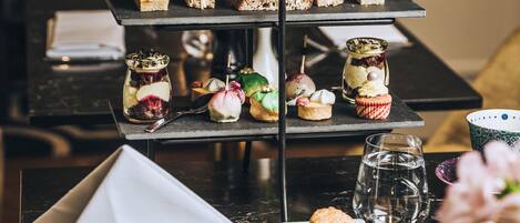 Una presentación de postres de tres niveles con diversos pasteles y pequeñas porciones, una tetera y una taza de té sobre una mesa.