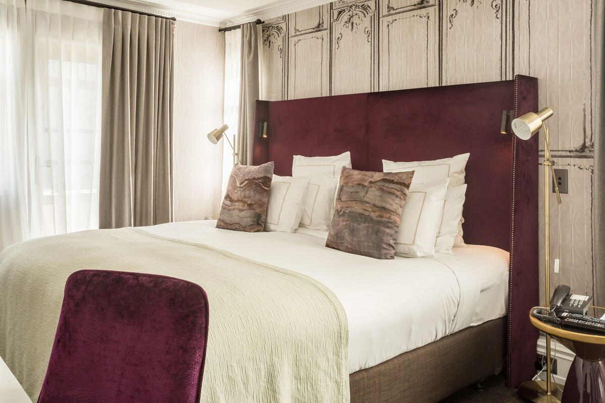 Une chambre d’hôtel avec un grand lit, une tête de lit rouge et un bureau avec une lampe.