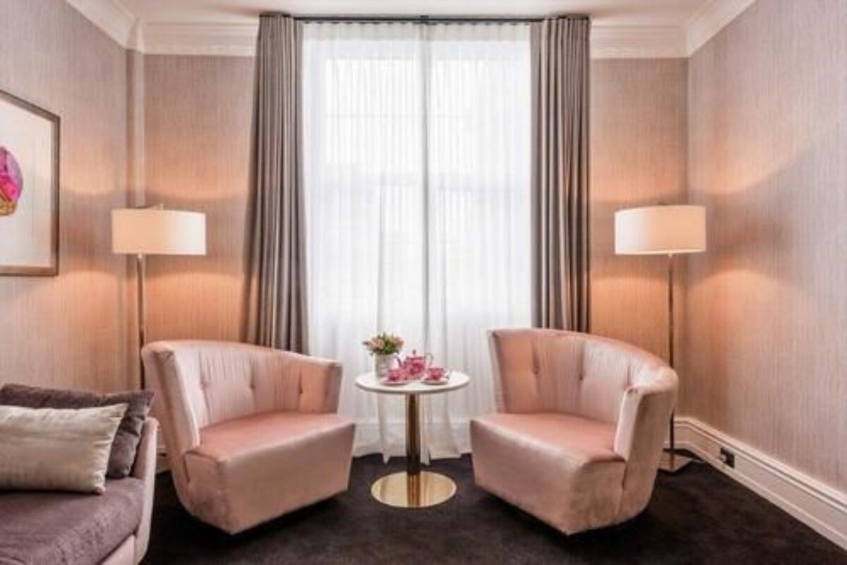 Une chambre d’hôtel avec deux fauteuils, une petite table ronde ornée d’un vase de fleurs et deux lampes.