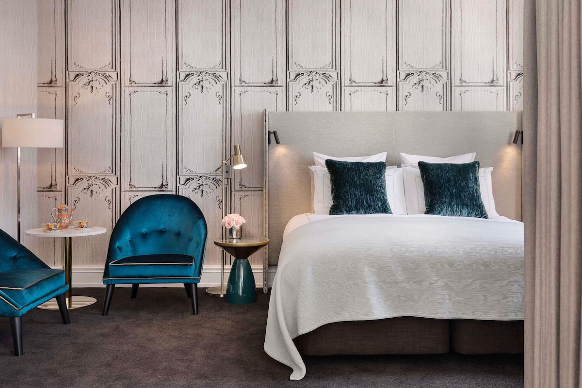 A hotel room with a bed, a chair, a small table, and a lamp.