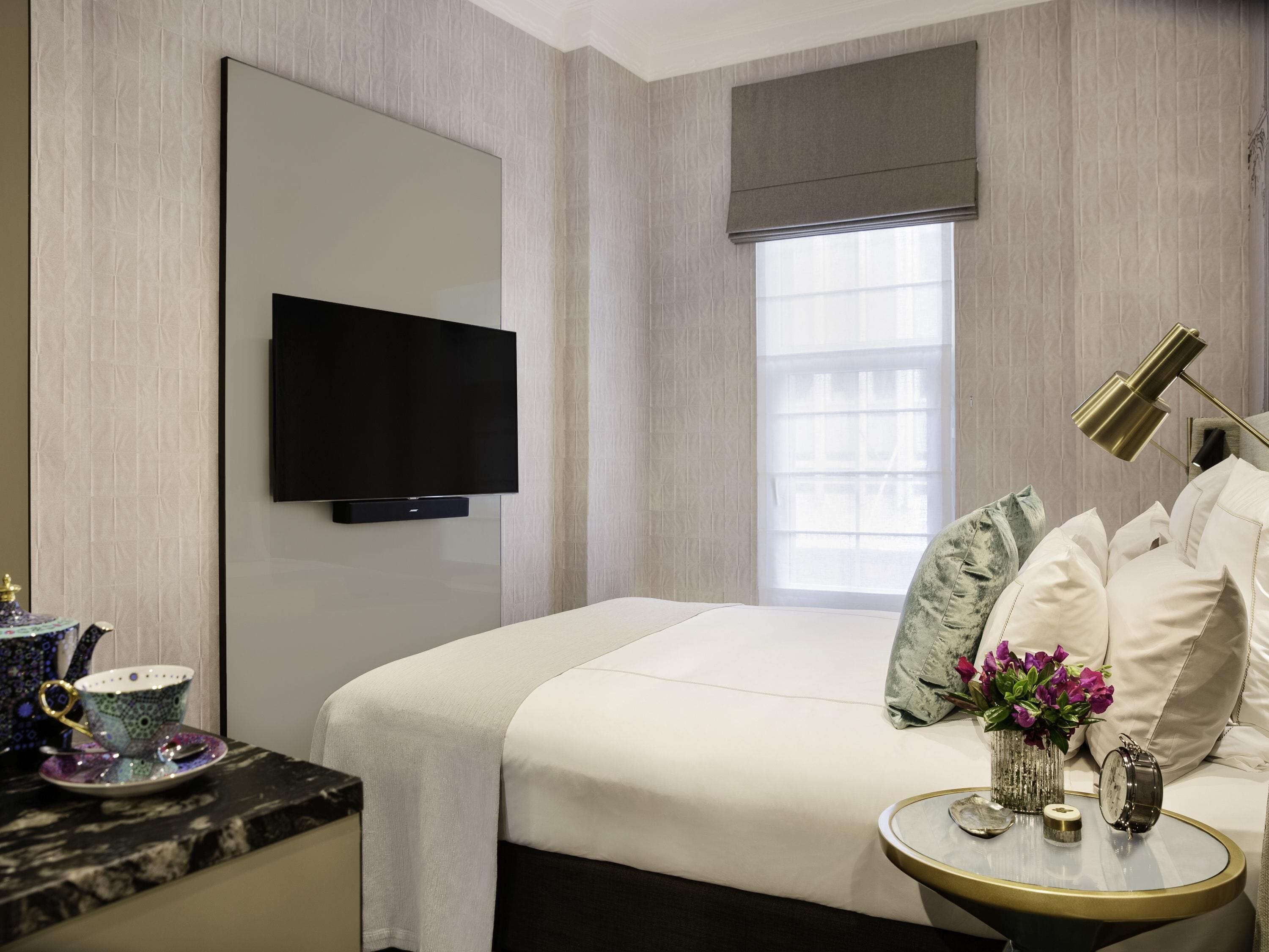 A hotel room with a bed, a television, a bedside table with a lamp, and a window with a view.