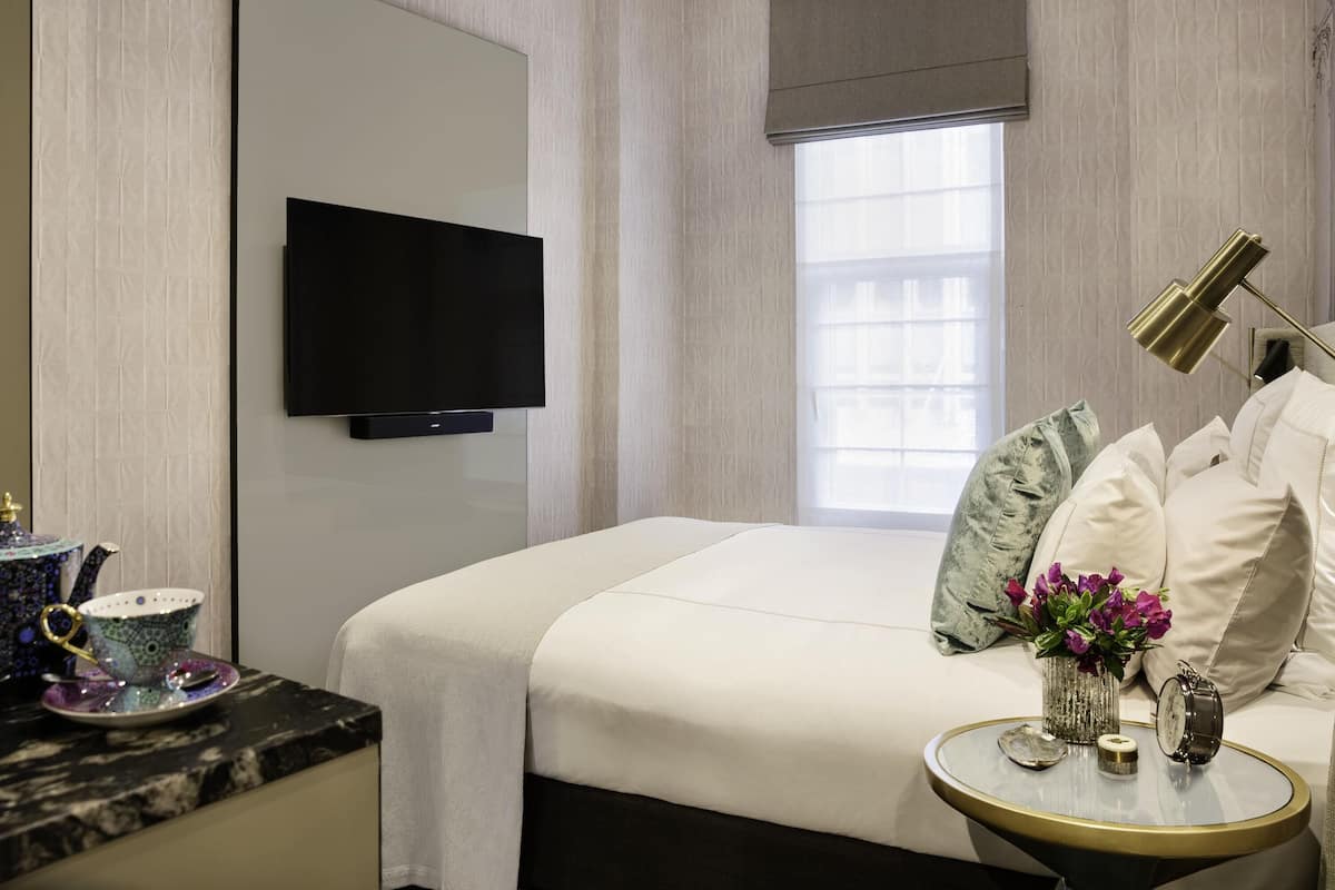A hotel room with a bed, a television, a bedside table with a lamp, and a window with a view.