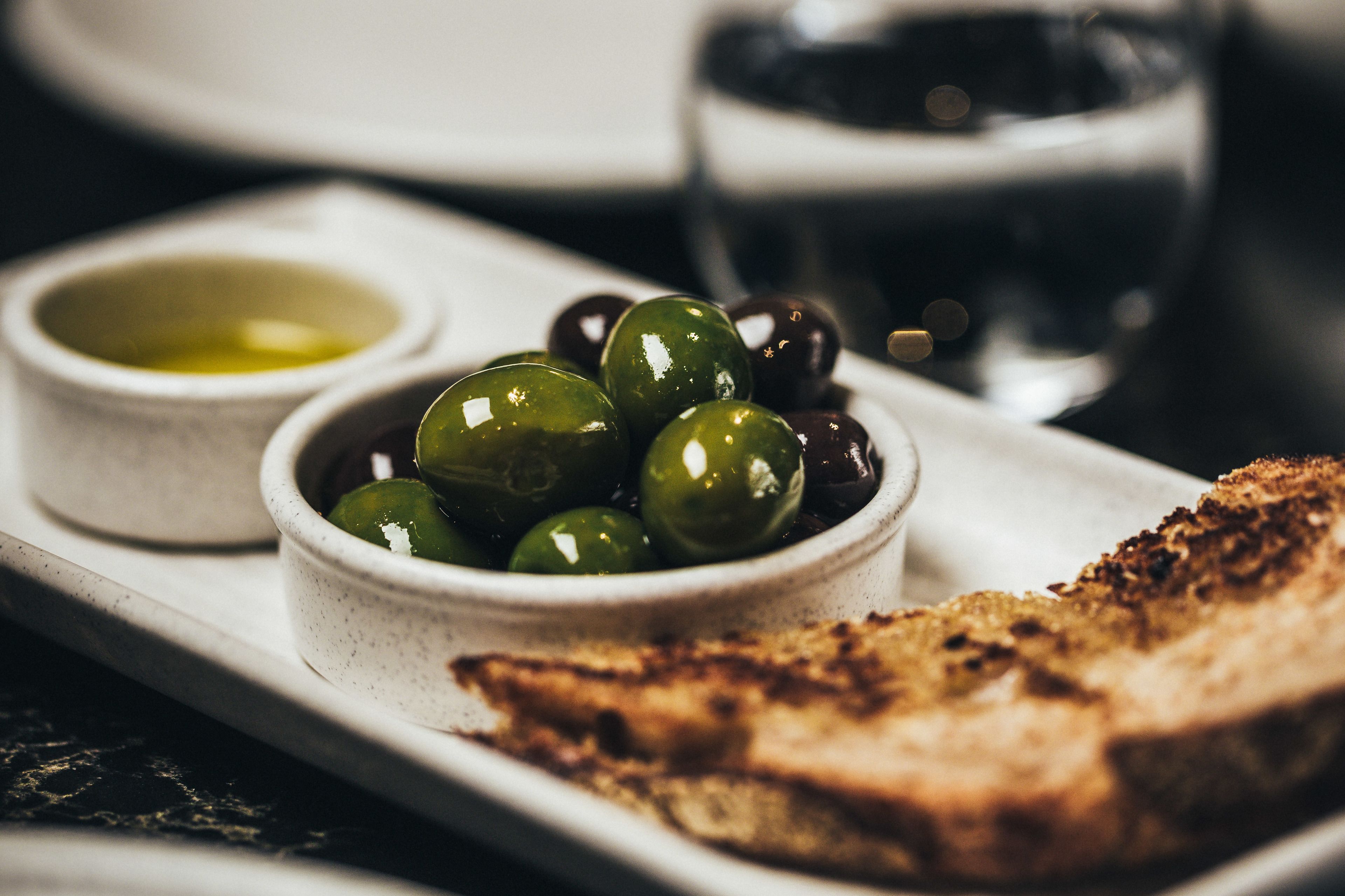 A plate with toasted bread, a bowl of olives, and a small bowl of olive oil.