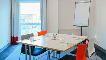 A conference room with a whiteboard, a table with chairs, and a view of the outside through large windows.