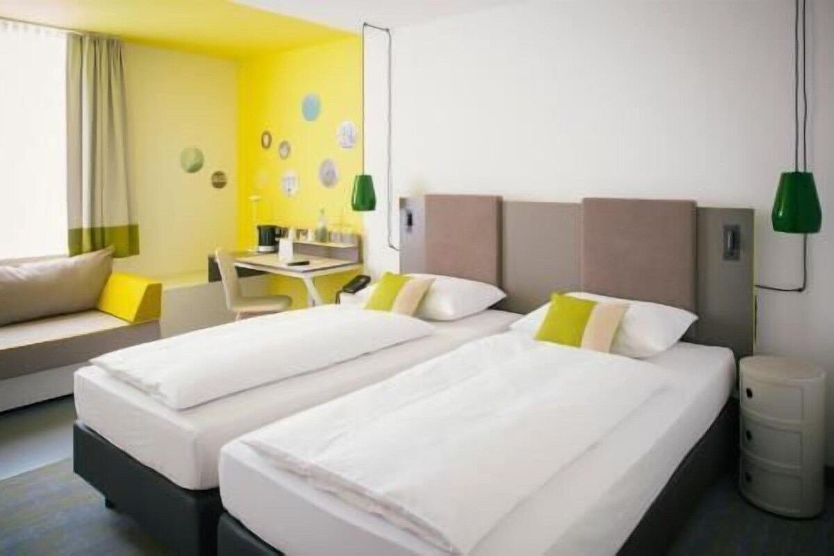 A hotel room with two beds, a desk, a chair, and a sofa.