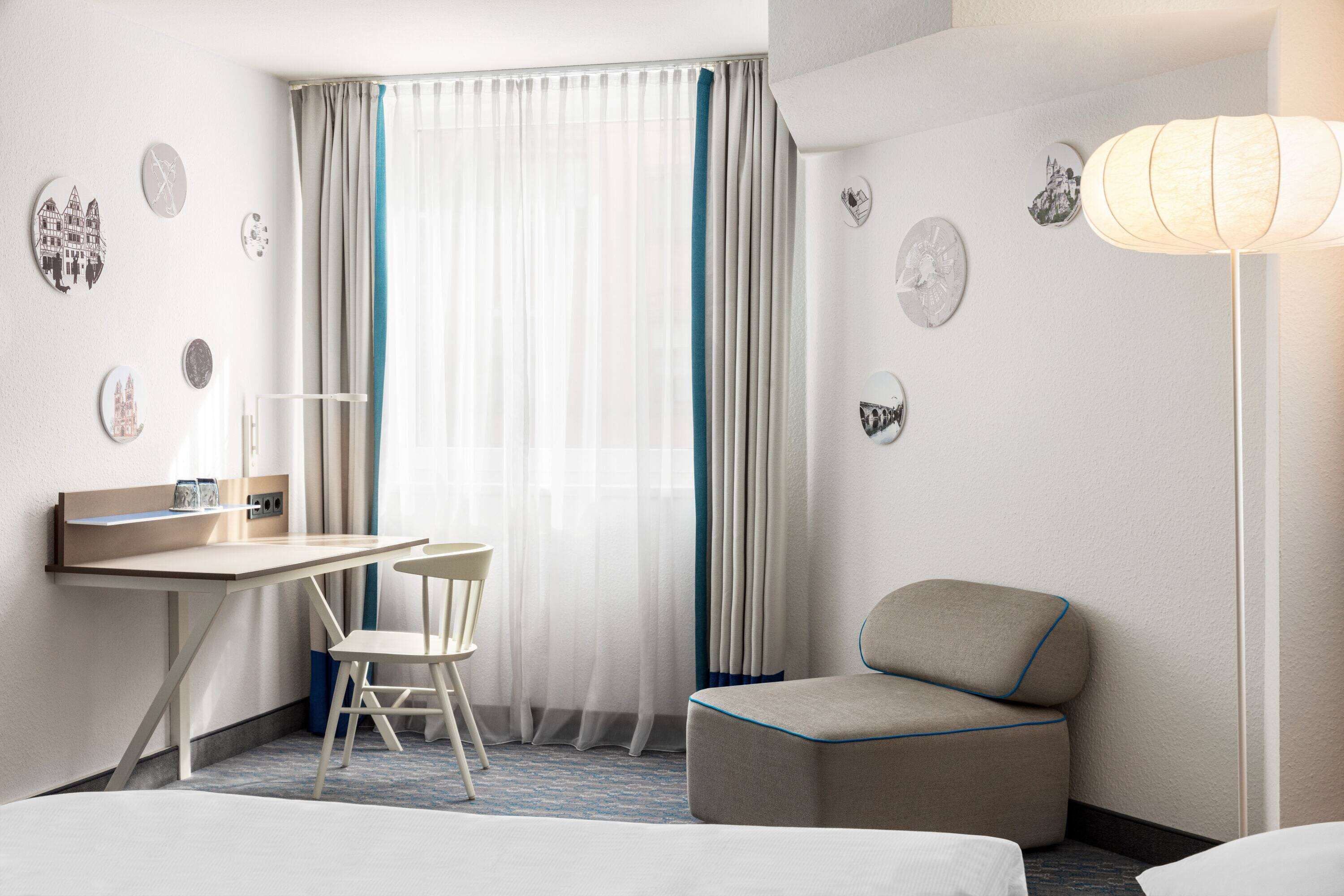 Een hotelkamer met een bureau, stoel en een klein voetenbankje.