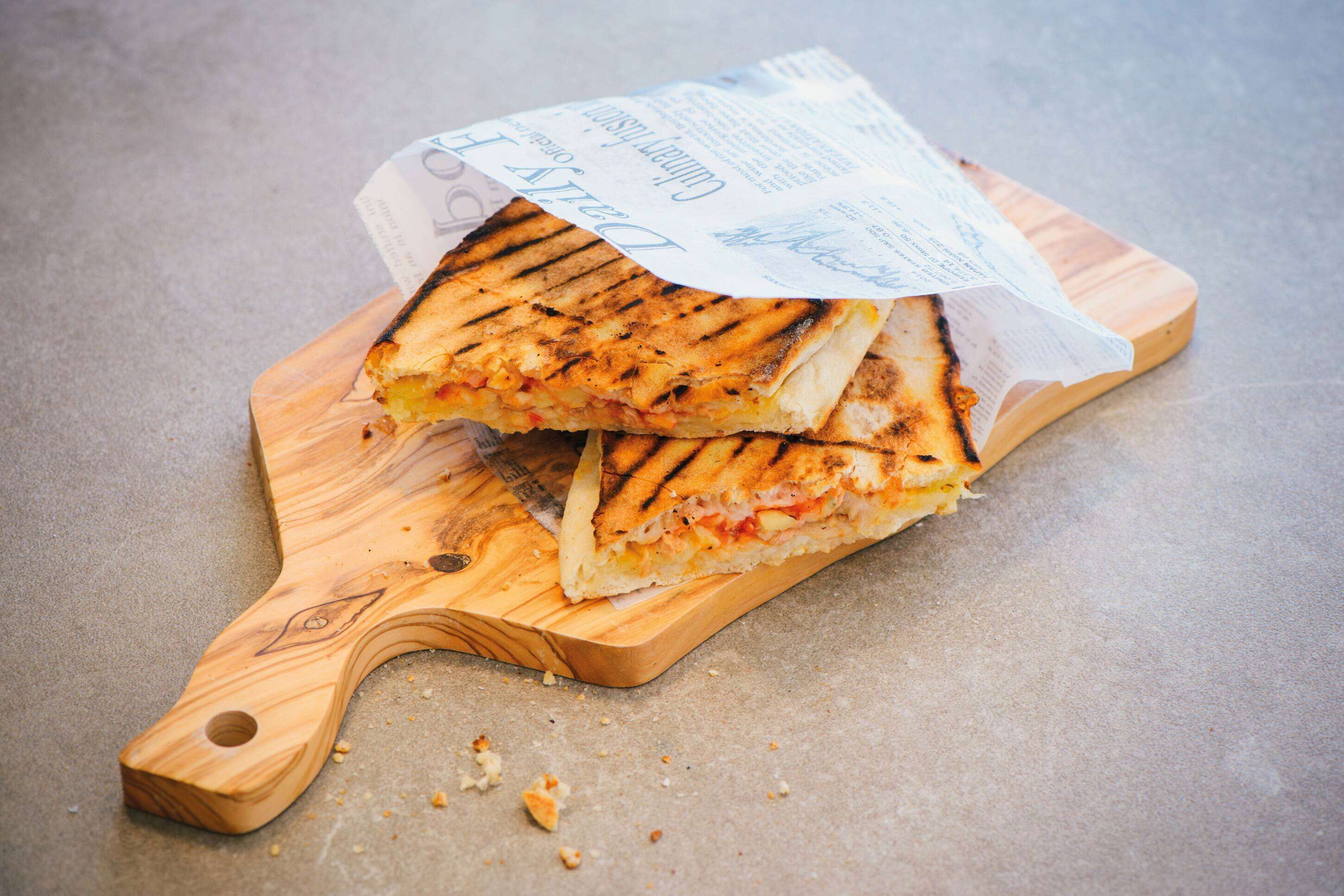 A grilled sandwich on a wooden cutting board with a receipt on top.