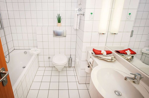 A bathroom with a bathtub, toilet, sink, and a mirror. - Vienna House Easy by Wyndham Limburg (Limburg an der Lahn)