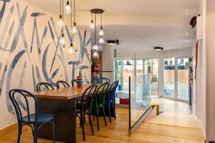 Uma sala de jantar moderna com mesa de madeira, cadeiras coloridas e luminárias pendentes.