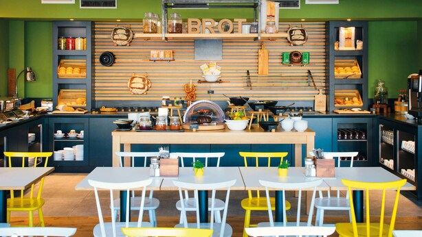 Een restaurant met een houten toonbank, planken met potten en keukengerei, en tafels met stoelen.