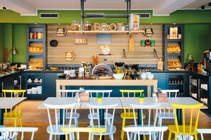 Un restaurant avec un comptoir en bois, des étagères remplies de bocaux et d’ustensiles de cuisine, et des tables avec des chaises.