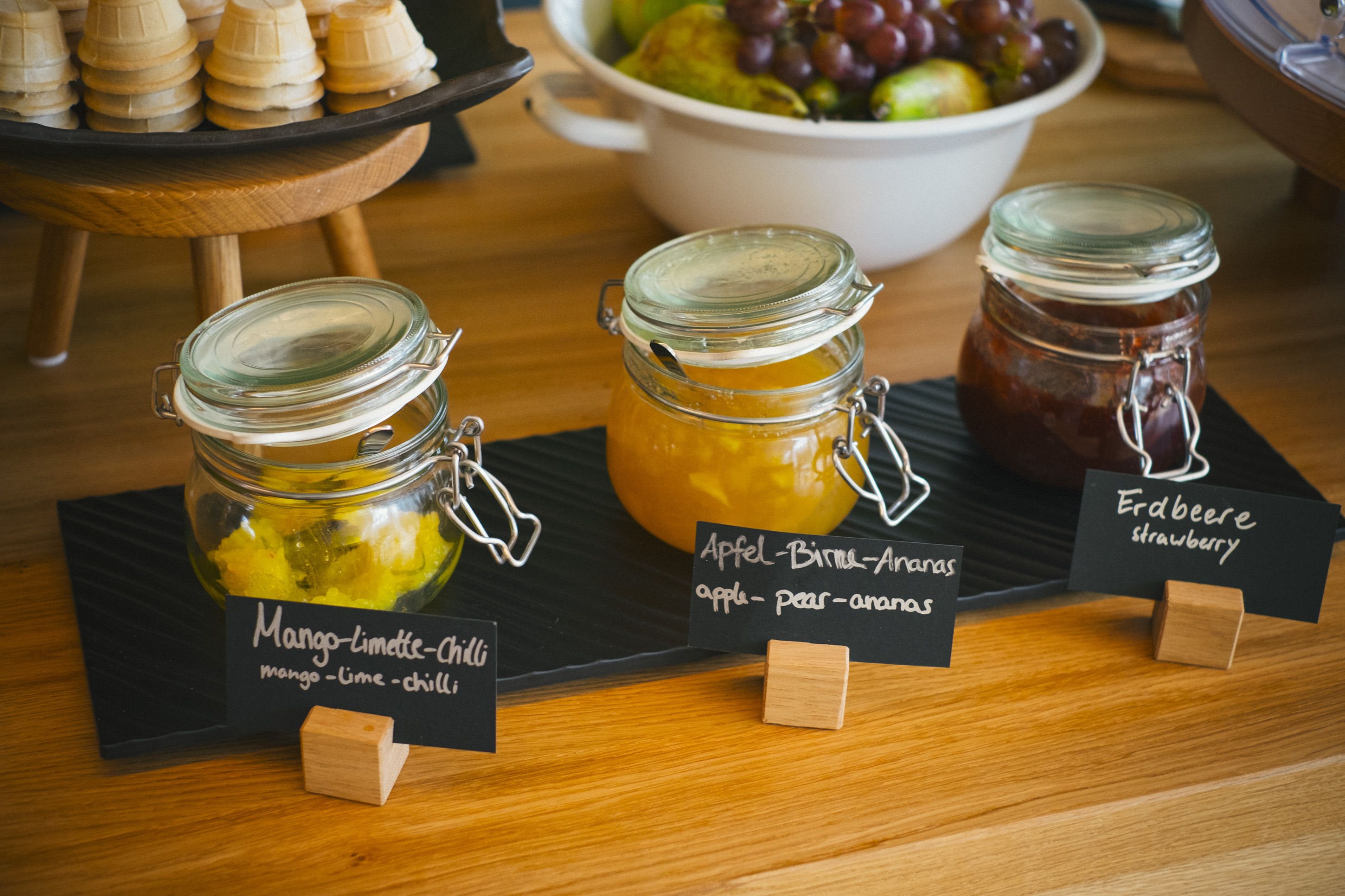 Three jars of preserves on a wooden table with labels.