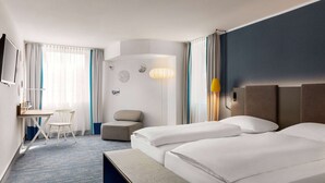 Een hotelkamer met twee bedden, een bureau, een stoel en een kleine zithoek.