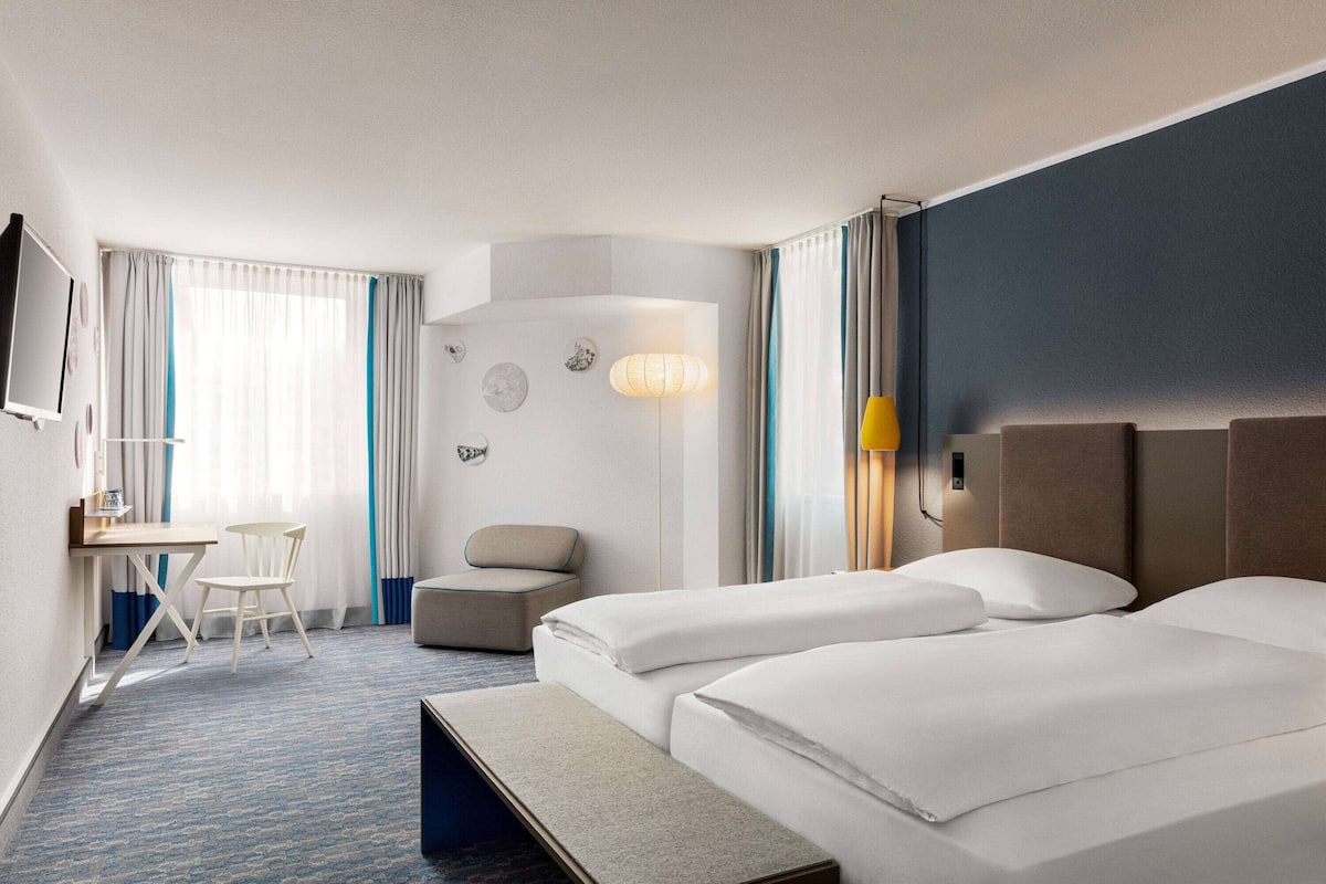 Une chambre d’hôtel avec deux lits, un bureau, une chaise et un petit canapé.