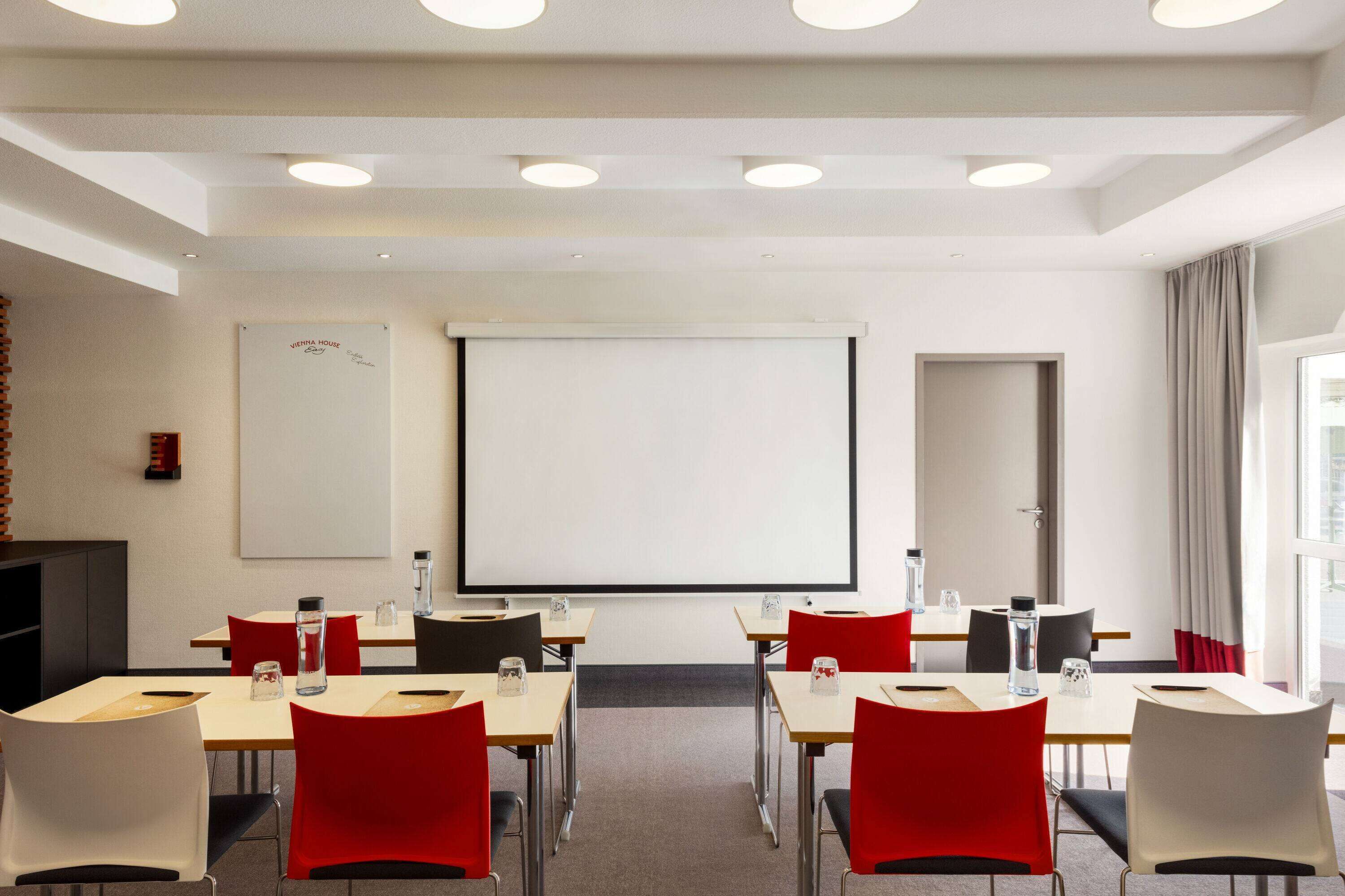 A conference room with a large screen, tables, and chairs.